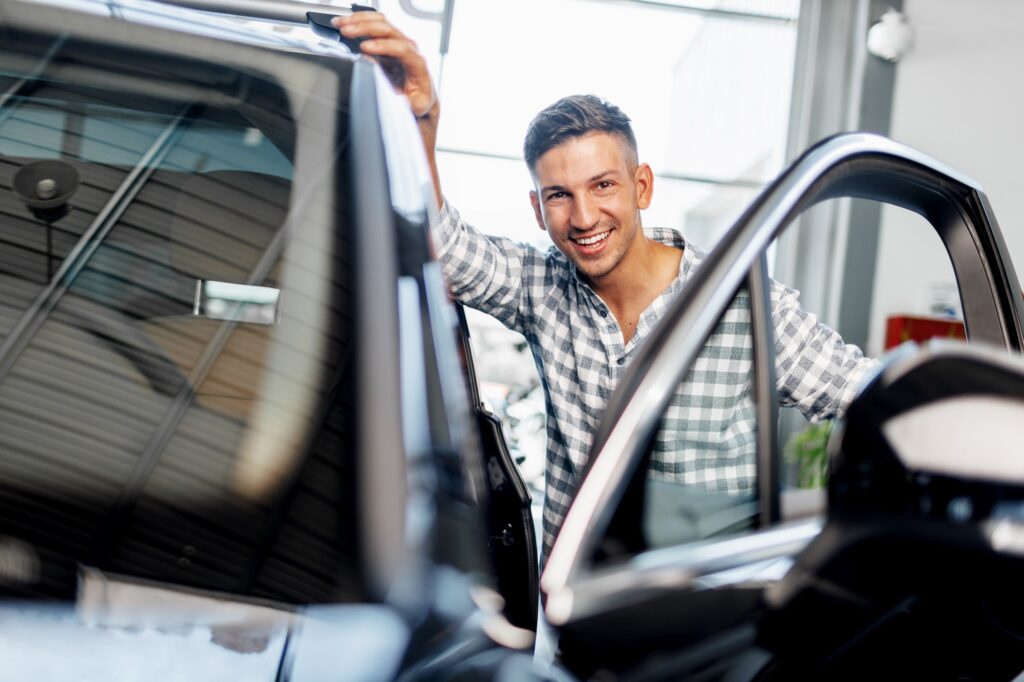 Cheerful young man customer buys a new car in a dealership