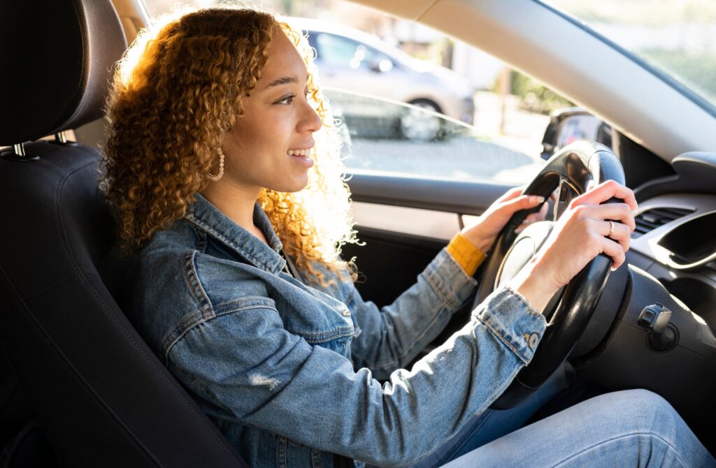 pretty hispanic curly haired woman driving a car happy at sunset